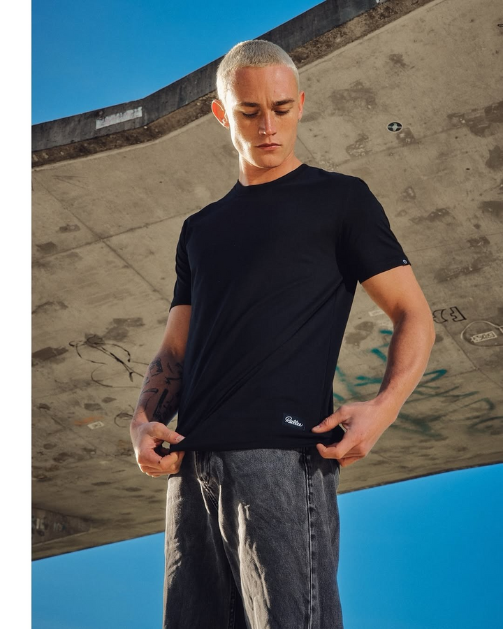 Man in a black t-shirt and grey jeans under a concrete overpass